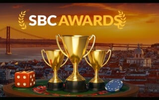 Golden trophies on a roulette table with dice and poker chip, Lisbon skyline and SBC Awards logo in the background