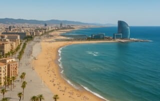 A panoramic view of Barcelona’s beachfront showing the W Hotel, golden sands, and the Mediterranean Sea under clear blue skies.